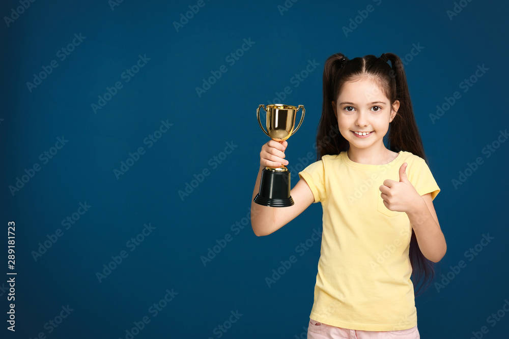 Happy girl with golden winning cup on dark blue background. Space for text Happy girl with golden winning cup on dark blue background. Space for text