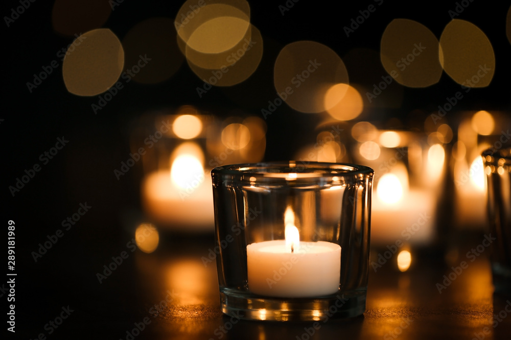 Burning candle on table against blurred background. Funeral symbol
