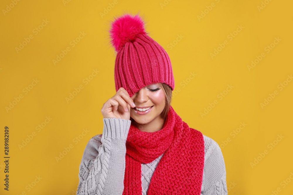 Obraz premium Funny young woman in warm sweater, scarf and hat on yellow background. Winter season