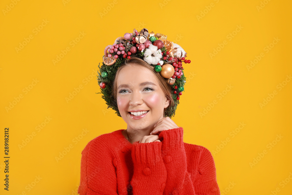 Beautiful young woman wearing Christmas wreath on yellow background Beautiful young woman wearing Christmas wreath on yellow background