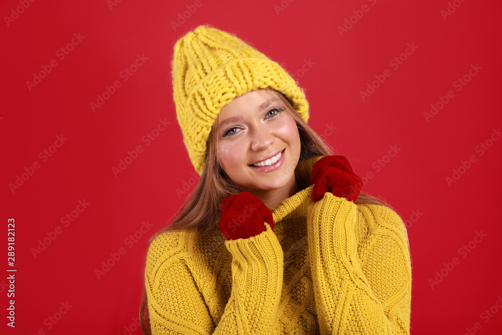 Young woman in warm sweater, gloves and hat on red background. Winter season