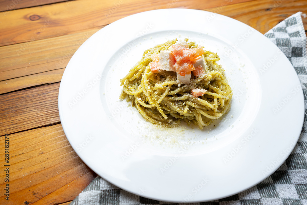 Spaghetti pasta with green pesto and cheese on wooden background