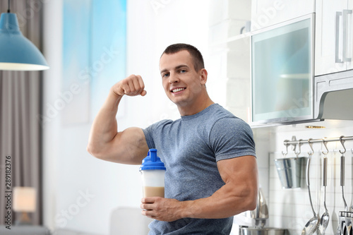 Athletic young man with protein shake in kitchen