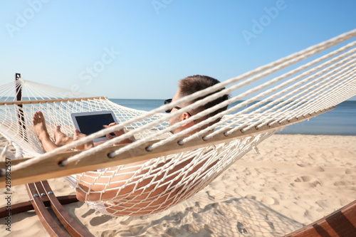 Young man with tablet in hammock on beach