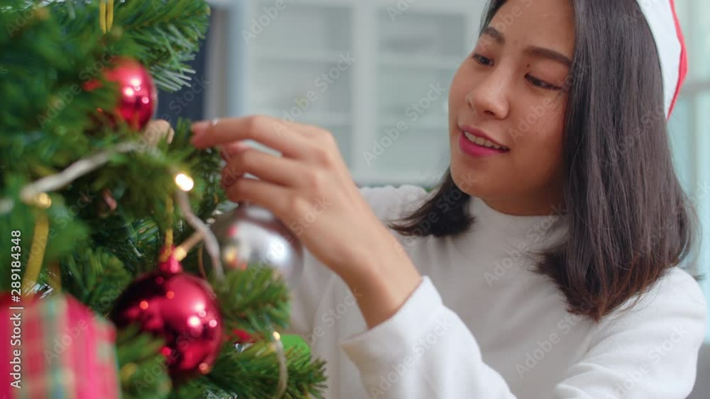 Asian women decorate Christmas tree at Christmas festival. Female teen happy smiling celebrate xmas winter holidays in living room at home. Close up shot. Asian women decorate Christmas tree at Christmas festival. Female teen happy smiling celebrate xmas winter holidays in living room at home. Close up shot.