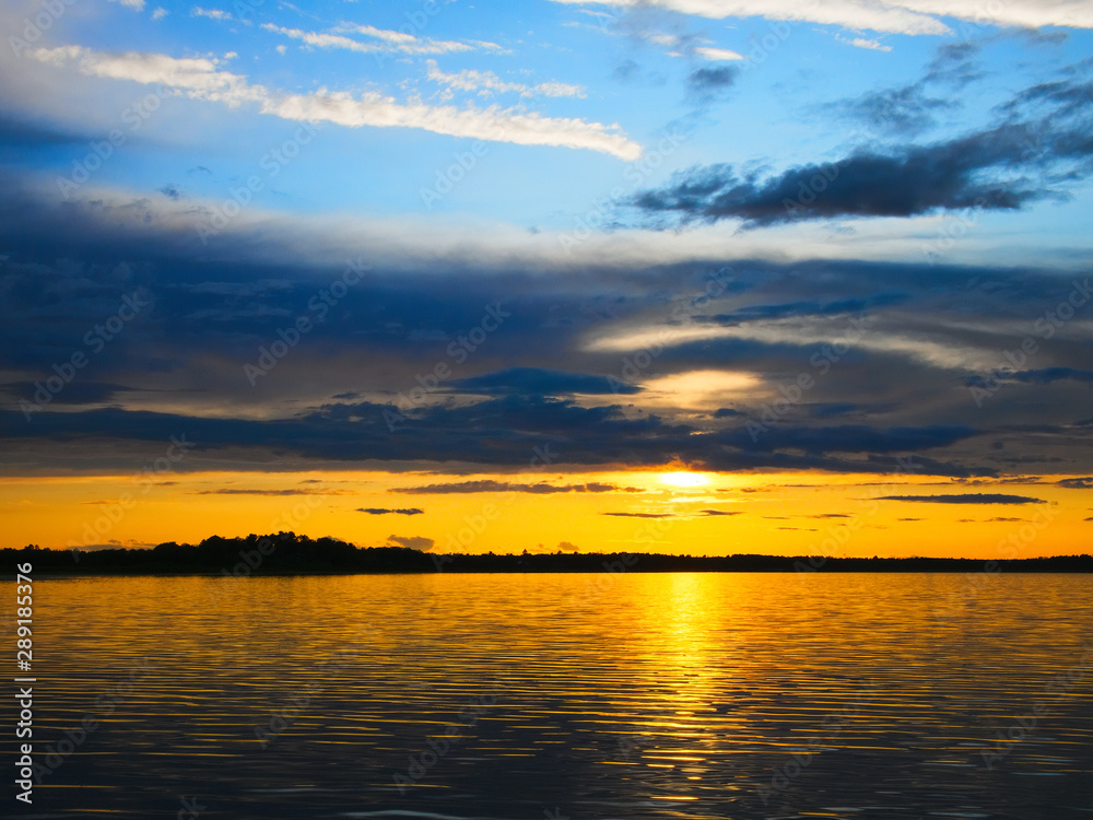 Setting sun hides behind clouds in beautiful sunset in blue and gold over Lake Irving in Bemidji Minnesota on a summer evening. Setting sun hides behind clouds in beautiful sunset in blue and gold over Lake Irving in Bemidji Minnesota on a summer evening.