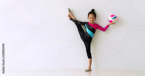 Acrobat little cute girl standing one leg while holding color ball in her hand in the room on white background. Lovely child girl doing gymnastics balance her body on the floor. Exercise concept.