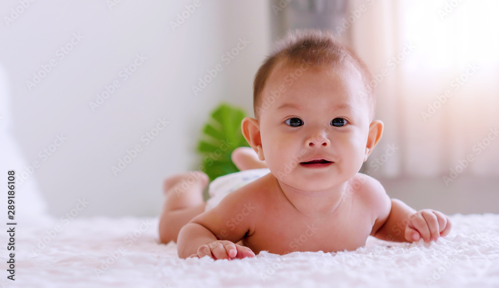 Cheerful cute baby lying and relax on white bed looking at something or family. Newborn boy wear diapers playing on the bed at home. Cheerful cute baby lying and relax on white bed looking at something or family. Newborn boy wear diapers playing on the bed at home.