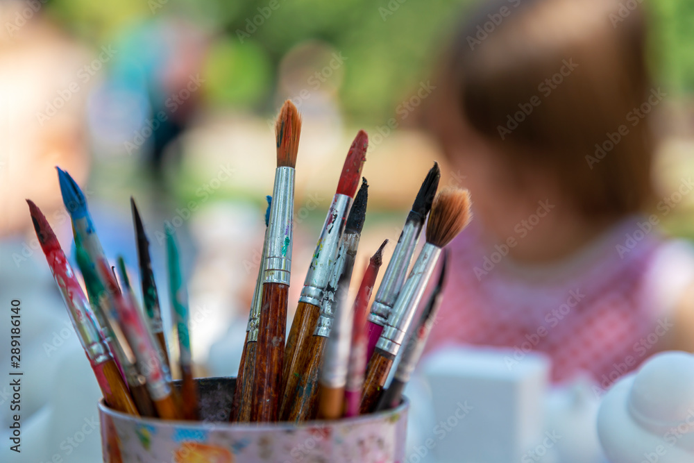 Fototapeta premium Children in the park paint with brushes and watercolors. Close-up of paintbrushes on blurred background. Image