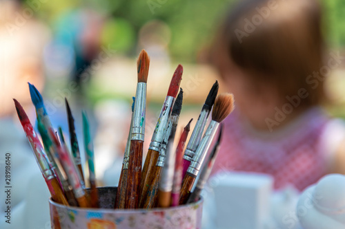 Children in the park paint with brushes and watercolors. Close-up of paintbrushes on blurred background. Image