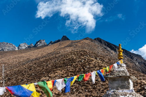 Colourful prayer flags hang on a Buddhist structure in the brown Nepalese mountain side with a cloud looming above