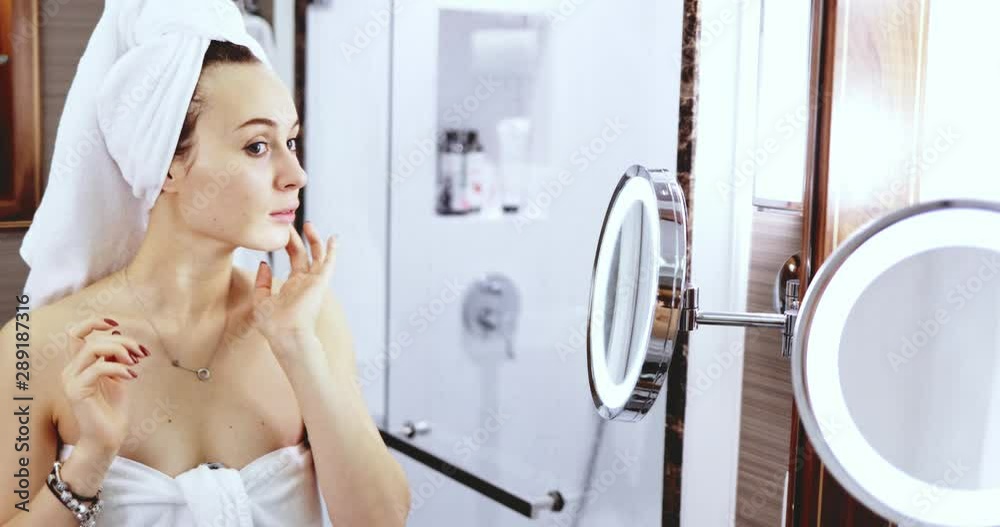 Young Woman Applying Make Up. SLOW MOTION. Girl apply nude eye shadow with brush, standing before the mirror in the bathroom after shower. Everyday beauty rituals.