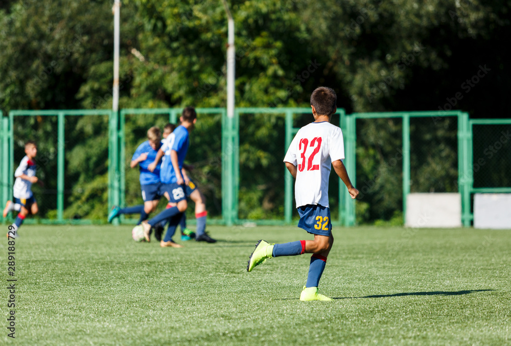 Obraz premium Boys in white and blue sportswear plays football on field, dribbles ball. Young soccer players with ball on green grass. Training, football, active lifestyle for kids concept 