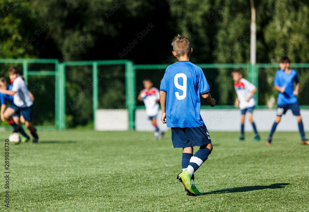 Boys in white and blue sportswear plays  football on field, dribbles ball. Young soccer players with ball on green grass. Training, football, active lifestyle for kids concept 