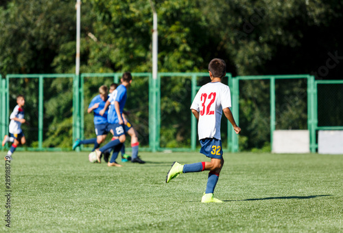 Boys in white and blue sportswear plays  football on field  dribbles ball. Young soccer players with ball on green grass. Training  football  active lifestyle for kids concept 