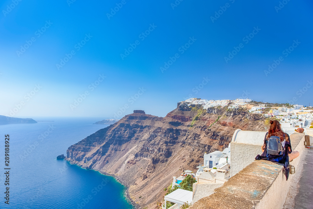 Young Woman on Parapet in Front of Panoramic View of Thira City in Santorini Island in Greece.