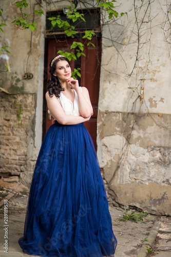 Tranquil Caucasian Lady in Long Blue Dress and Tiara Posing in Authentic Yard Outdoors.
