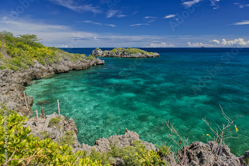 Beautiful cove rocky shoreline and crystal clear turquoise ocean water in a hot summer bright day light and cloudy sky. Malapascua, Philippines.