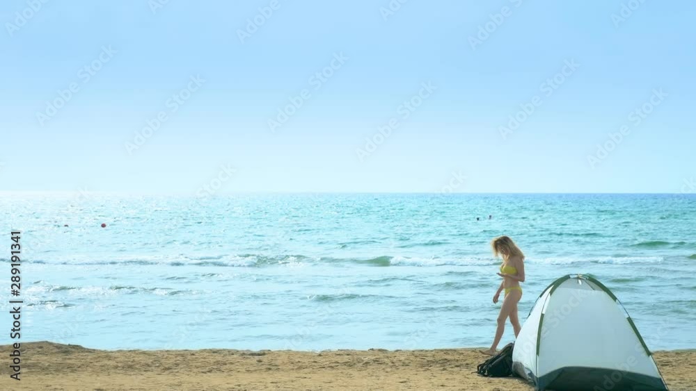Camping concept by the sea. Girl collects shells on the beach near the tent on a background of the sea. Camping concept by the sea. Girl collects shells on the beach near the tent on a background of the sea.
