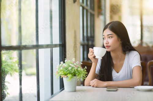 Φωτογραφία A beautiful woman who is sitting drinking coffee near the window with warm sunlight passing through in the morning