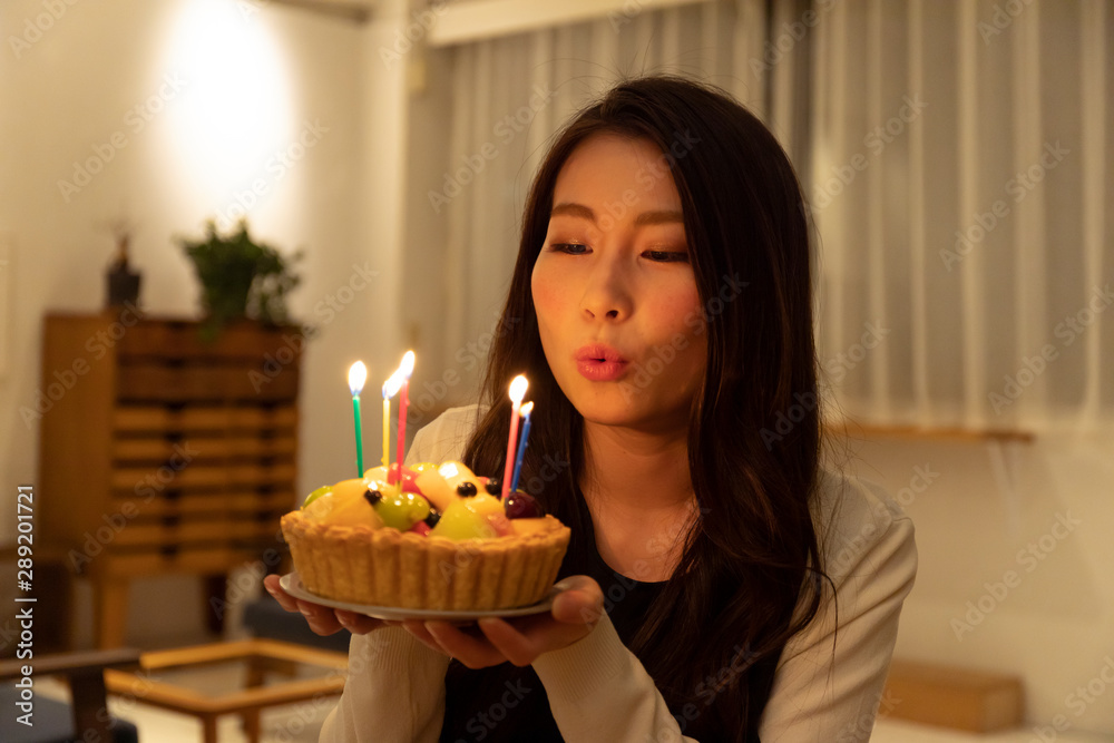 部屋の中でロウソクに火のついたケーキを持つ若い女性 部屋の中でロウソクに火のついたケーキを持つ若い女性