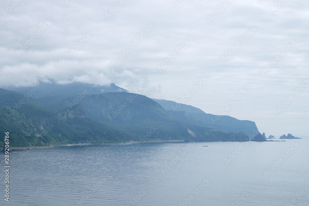 Lake or river view along with green forest , green mountain cover of misty,  against white sky in Hokkaido, Japan