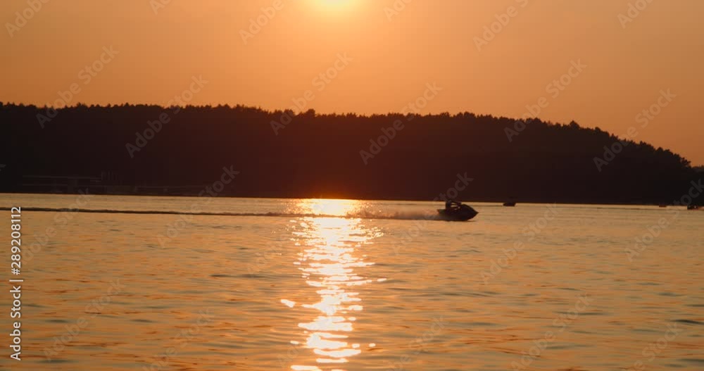 Motor boat speeds down the lake at sunset Motor boat speeds down the lake at sunset