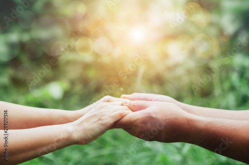 Close up of Two people holding hand together over blurred green nature garden background, Business man and woman shaking hands, helping hand and teamwork  concept with copy space © isara