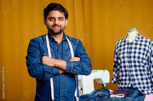 handsome indian tailor man In a stylish shirt working with dreen jeans cotton textile at home workshop yellow curtain background photo