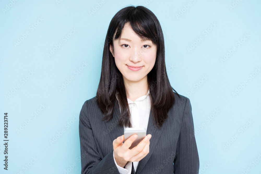 Young business woman holding smart phone against light blue background Young business woman holding smart phone against light blue background