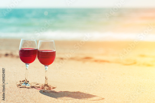 Two wine glasses with red wine on the sand of the beach at the sea shore. Romantic couple.