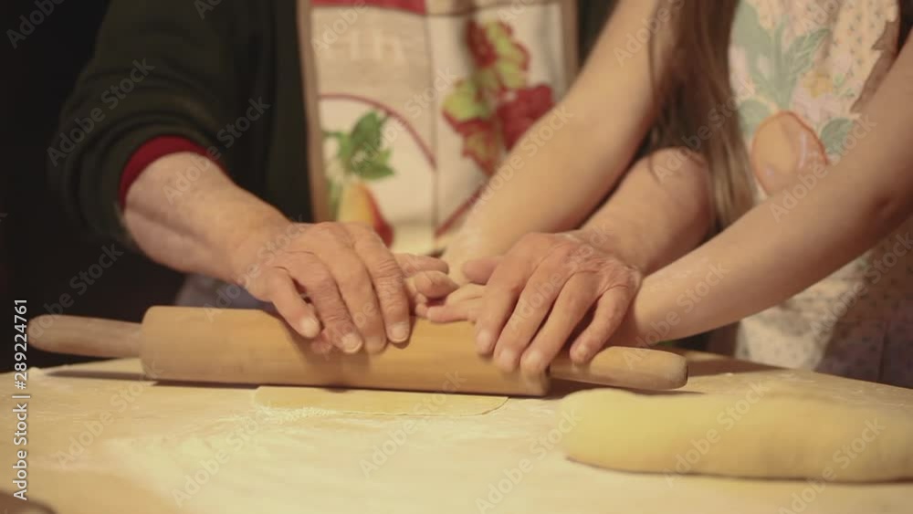 Grandmother teaching little girl to prepare a cake or pizza. Family cooking together. Hands close up on rolling pin and dough. Grandmother teaching little girl to prepare a cake or pizza. Family cooking together. Hands close up on rolling pin and dough.