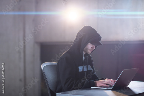 young talented hacker using laptop computer while working in dark office