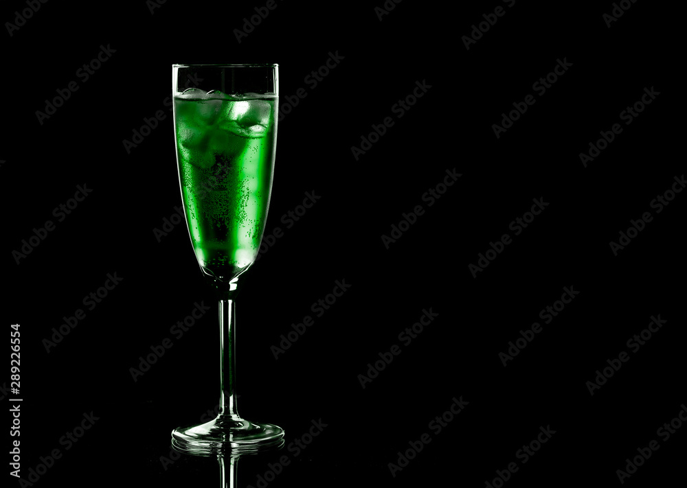 Glass of green champagne with ice on black background