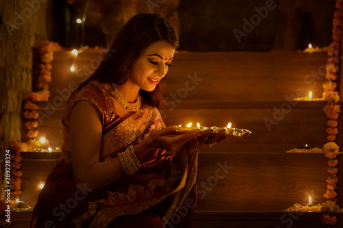 young woman sitting on stairs with diyas in hand	 photo