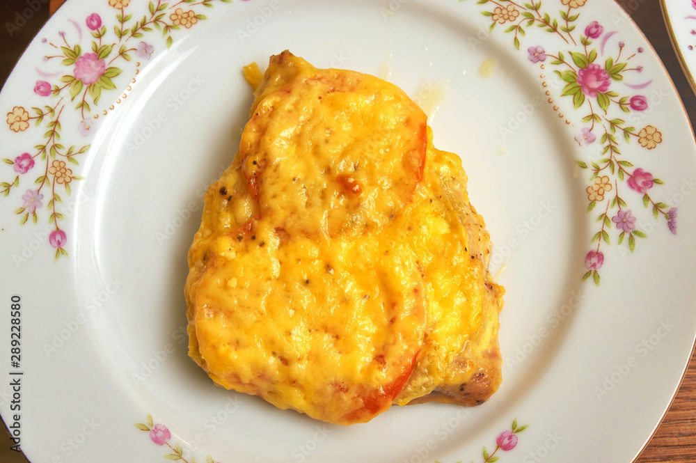 Baked meat with tomatoes and cheese on a white plate, view from the top close up