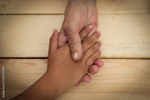 Hands of an elderly man hold the hands of a child. The concept of care and help for old people, the connection of the older and younger generation of people. Image.