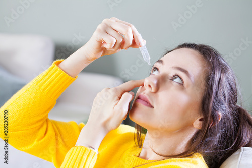 Fotografia Closeup view of young woman applying eye drop, artificial tears..