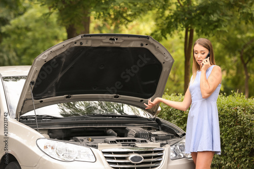 Woman calling her insurance agent while standing near broken car on road © Pixel-Shot