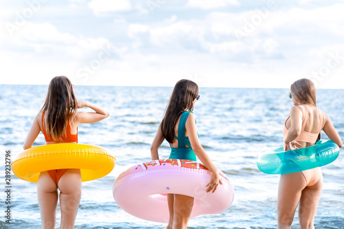 Beautiful young women with swimming rings on sea beach at resort