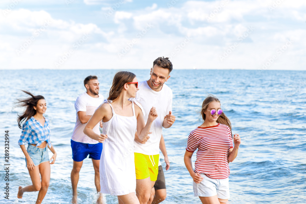 Happy friends running on sea beach at resort