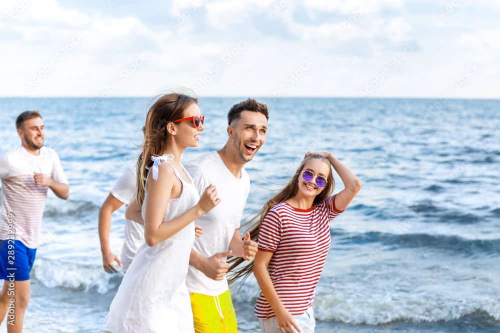 Happy friends running on sea beach at resort