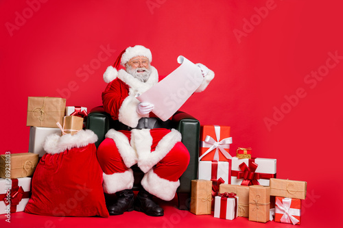 Fotografie Nice cheerful cheery hard-working fat bearded man St Nicholas sitting in armchai