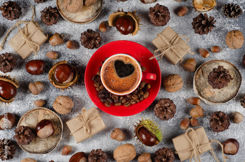 Autumn composition. Сup of coffee on autumn pattern of chestnuts, cones, acorns, nuts, gift boxes on a gray shabby background. © Iryna Ustynchenko