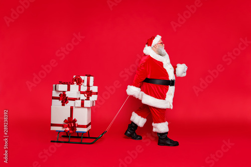 Full length body size profile side view of nice hard-working fat bearded man delivering carrying many heavy different purchases shop isolated on bright vivid shine red background