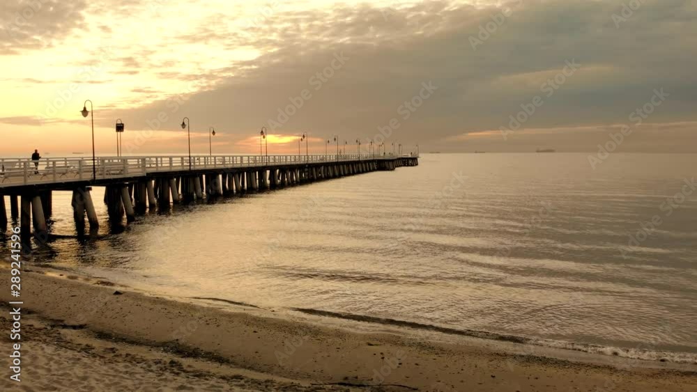 Beautiful aerial shot sunrise by the sea. A calm sea with smooth waves. Orange sky and clouds in the bright sky. A lonely man walks on the pier and takes pictures. Gdynia Orłowo, Poland Beautiful aerial shot sunrise by the sea. A calm sea with smooth waves. Orange sky and clouds in the bright sky. A lonely man walks on the pier and takes pictures. Gdynia Orłowo, Poland