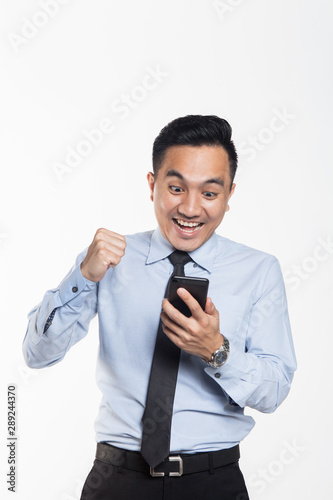 Asian man in office wear looking at his handphone with being success expression
