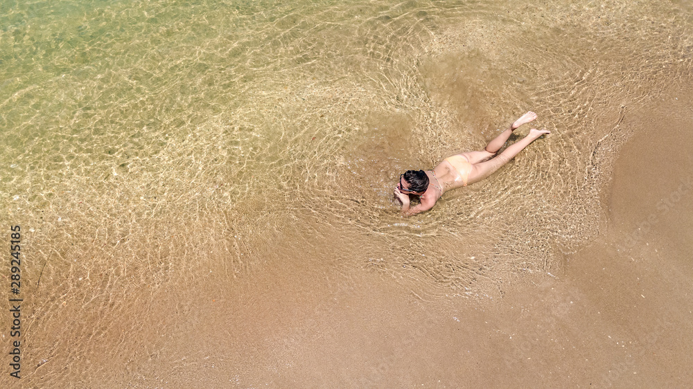 Aerial top view of young woman in bikini relaxing on sand tropical beach by sea and waves from above, girl on tropical island beach vacation in Thailand