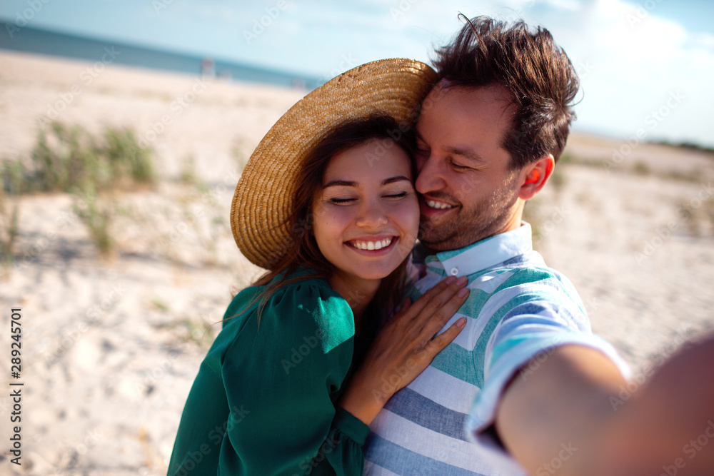Happy traveling couple in love taking a selfie on phone at the beach on a sunny summer day.