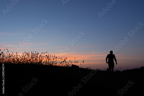 Silhouette of a man walking at sunset over a field of wheat. Landscape with a silhouette of a guy. Deep sunset and traveler.